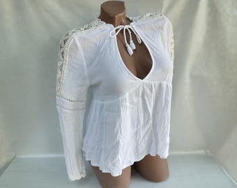 May include: White long-sleeve blouse with a lace trim on the shoulders and sleeves. The blouse has a keyhole neckline with a tie closure.