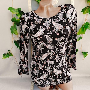 Peut inclure: Un haut noir à manches longues orné d'un motif répétitif de formes cachemire blanches entremêlées de petites grappes de fleurs roses et bleues. Le vêtement présente une encolure ronde et un ourlet droit, avec un imprimé uniforme sur l'ensemble.