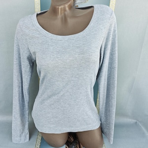 Op de afbeelding: Een lichtgrijs shirt met lange mouwen en een ronde hals. Het shirt is gemaakt van een geribbelde gebreide stof. Het kledingstuk wordt op een mannequin getoond.