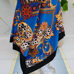 Puede incluir: Un pa&ntilde;uelo azul con borde negro, con un dise&ntilde;o de cadena dorada y floral con detalles de estampado de leopardo. El pa&ntilde;uelo es de material sedoso y est&aacute; drapeado sobre una superficie.