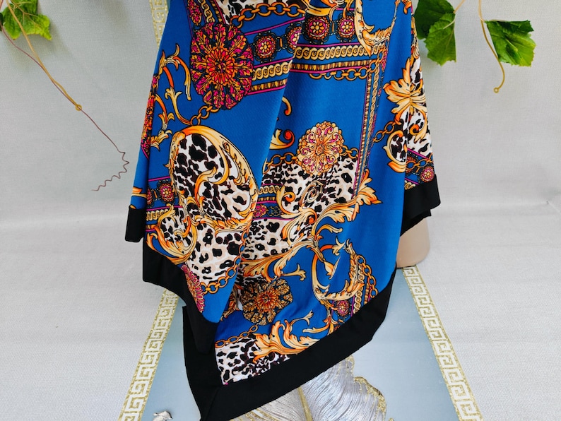 Puede incluir: Un pa&ntilde;uelo azul con borde negro, con un dise&ntilde;o de cadena dorada y floral con detalles de estampado de leopardo. El pa&ntilde;uelo es de material sedoso y est&aacute; drapeado sobre una superficie.