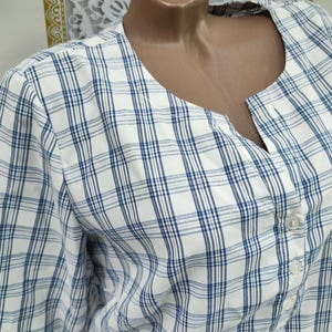 Pu&ograve; includere: Camicia a quadri bianchi e blu con scollatura a V e chiusura con bottoni. La camicia a maniche corte presenta un classico motivo a quadri in bianco e blu navy. Realizzata in tessuto leggero.
