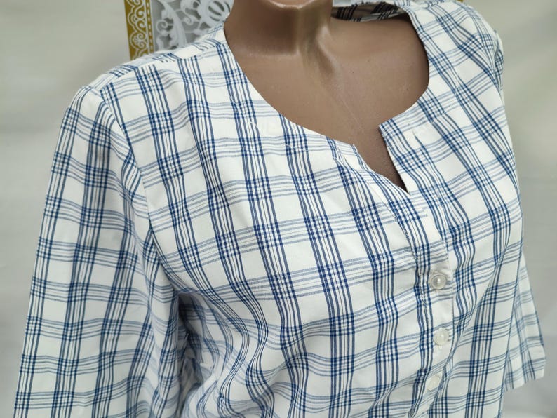 Pu&ograve; includere: Camicia a quadri bianchi e blu con scollatura a V e chiusura con bottoni. La camicia a maniche corte presenta un classico motivo a quadri in bianco e blu navy. Realizzata in tessuto leggero.