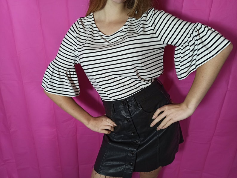 May include: A black and white striped shirt with bell sleeves and a black leather skirt with a button closure.