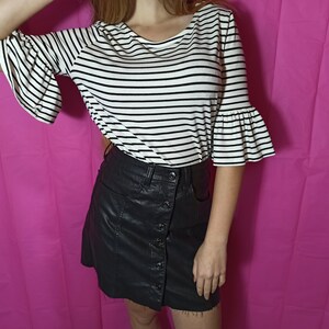 May include: A black and white striped shirt with a ruffled sleeve and a black faux leather skirt with a button closure.