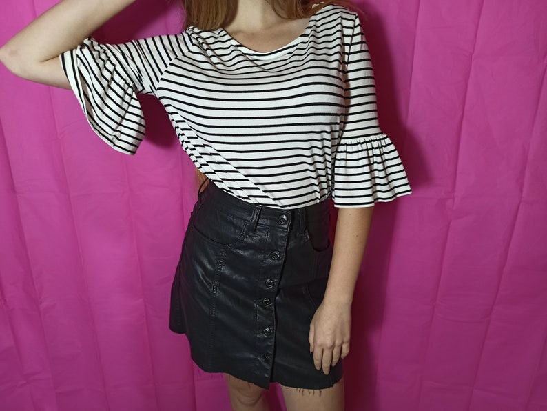 May include: A black and white striped shirt with a ruffled sleeve and a black faux leather skirt with a button closure.