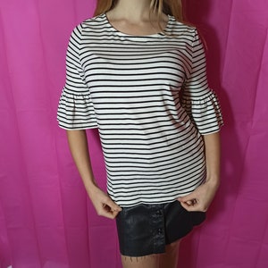 May include: A white and black striped shirt with short, ruffled sleeves. The shirt has a round neckline and is made of a soft, stretchy fabric.