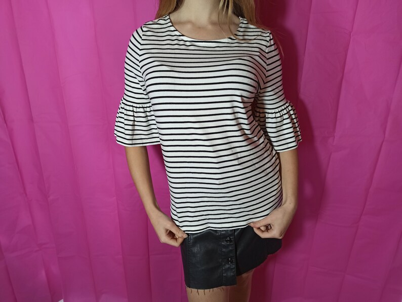 May include: A white and black striped shirt with short, ruffled sleeves. The shirt has a round neckline and is made of a soft, stretchy fabric.