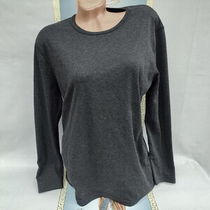 Peut inclure: Un haut à manches longues gris foncé avec un col rond. Le vêtement est présenté sur un mannequin. Le tissu semble être une matière tricotée douce. Les manches sont longues et le style général est décontracté.