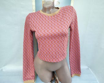 Puede incluir: Un suéter de manga larga recortado con un patrón geométrico rosa y naranja. El suéter tiene un cuello redondo y puños en un color beige contrastante. La prenda se exhibe en un maniquí.