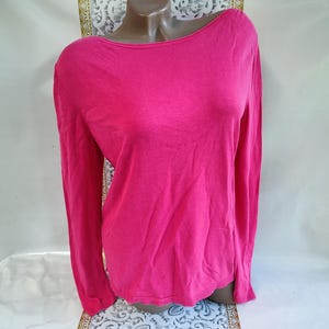 May include: A long-sleeved, hot pink shirt with a boat neck. The shirt is made of a soft material and has a simple, classic design. The sleeves are long and the hemline is straight. The shirt is displayed on a mannequin.