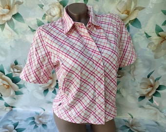 Puede incluir: Una camisa de manga corta con botones y un estampado de cuadros rosa y blanco. La camisa tiene un cuello clásico y un corte ligeramente recortado.
