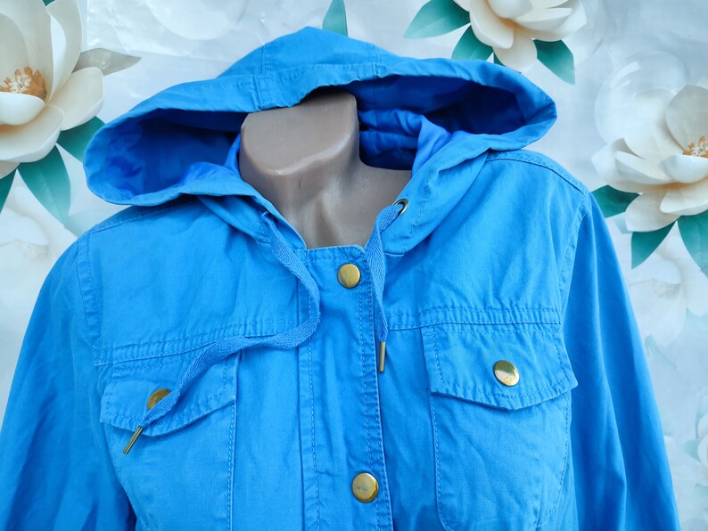 May include: A light blue hooded jacket with gold buttons and a drawstring closure.