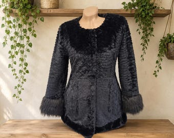 May include: A black textured coat featuring a round neckline, long sleeves with faux fur cuffs, and a front button closure. The garment has a dense, curly pile texture throughout the body, with a smooth, dark faux fur trim along the collar and hem.