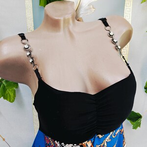 Puede incluir: Top negro con tirantes decorativos de pedrer&iacute;a. El top tiene un busto fruncido y se combina con una falda azul estampada. Los tirantes son negros con aros plateados y pedrer&iacute;a transparente.