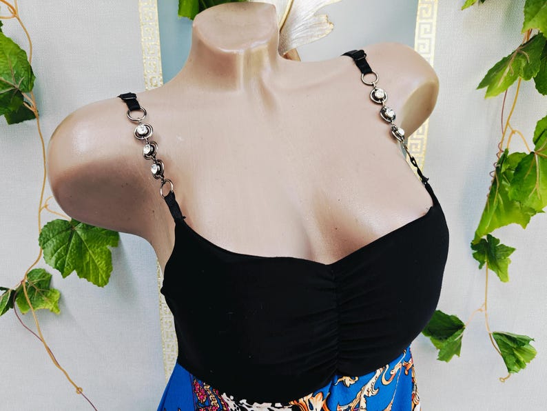 Puede incluir: Top negro con tirantes decorativos de pedrer&iacute;a. El top tiene un busto fruncido y se combina con una falda azul estampada. Los tirantes son negros con aros plateados y pedrer&iacute;a transparente.