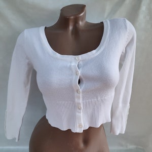 May include: White cropped cardigan with long sleeves and a button-up front.