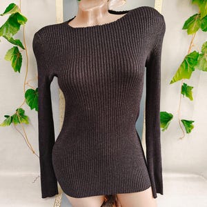 May include: A dark brown long-sleeve sweater featuring a vertical ribbed knit texture, a fitted silhouette, and a rounded neckline. The garment is constructed from a knit fabric that displays a subtle shimmer throughout the dark brown material.