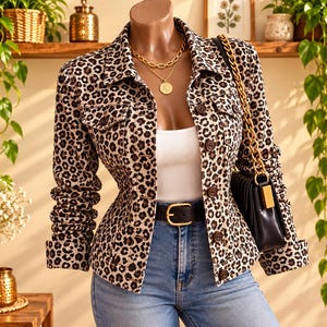 Puede incluir: Una chaqueta de mezclilla con estampado de leopardo, cuello, mangas largas y cierre frontal de botones. La chaqueta se lleva sobre una blusa blanca y pantalones vaqueros azules, complementada con un collar de cadena dorada y un bolso negro.