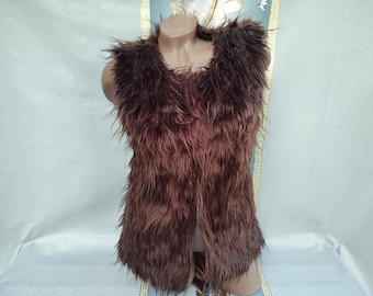May include: A brown faux fur vest with a V-neck design. The vest is sleeveless and has a shaggy texture. The garment is displayed on a mannequin.