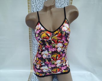 May include: A colorful camisole with a V-neck and spaghetti straps. The top features a vibrant print with images of a pop star, musical notes, and the word "GAGA". The trim is black, and the bottom hem has a black lace detail.