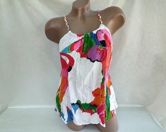 Puede incluir: Top blanco sin mangas con estampado floral colorido. El estampado presenta flores grandes en tonos de rosa, rojo, naranja, amarillo, verde y azul.