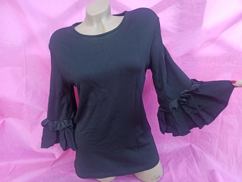 May include: Black long-sleeved shirt with ruffled bell sleeves. The shirt has a round neckline and is made of a soft, stretchy fabric.