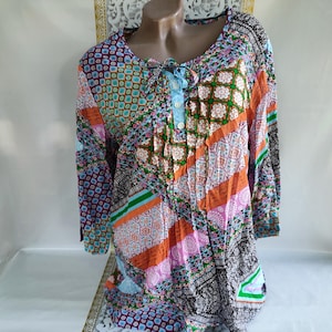 Op de afbeelding: Een patchwork blouse met lange mouwen, een ronde hals en een striksluiting. De blouse heeft een verscheidenheid aan kleurrijke patronen, waaronder bloemen, geometrische en abstracte ontwerpen in tinten blauw, oranje, roze en zwart.