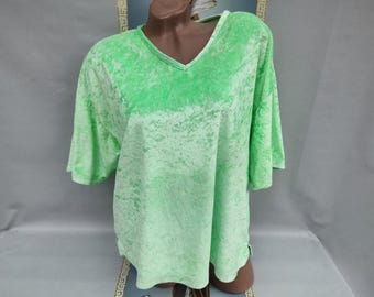 Puede incluir: Una camiseta verde claro con cuello en V y mangas cortas. La camiseta tiene un aspecto texturizado, similar al terciopelo. La tela tiene un efecto descolorido y moteado, con tonos de verde más claros y oscuros. La camiseta se muestra en un maniquí.