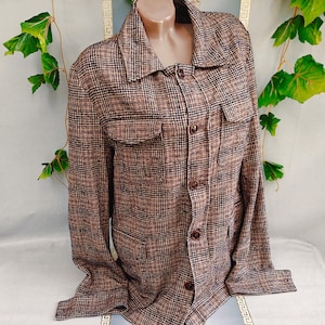 May include: A long-sleeved button-down shirt featuring a brown and black plaid pattern. The shirt includes a classic collar, a front button closure, and two chest pockets with flaps. The fabric has a textured appearance with a consistent grid design.