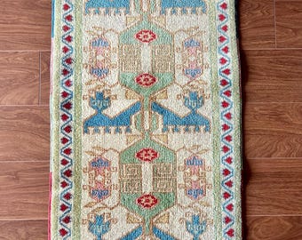 May include: A rectangular rug with a cream background and a geometric pattern in shades of blue, red, green, and yellow. The rug has a fringe border.