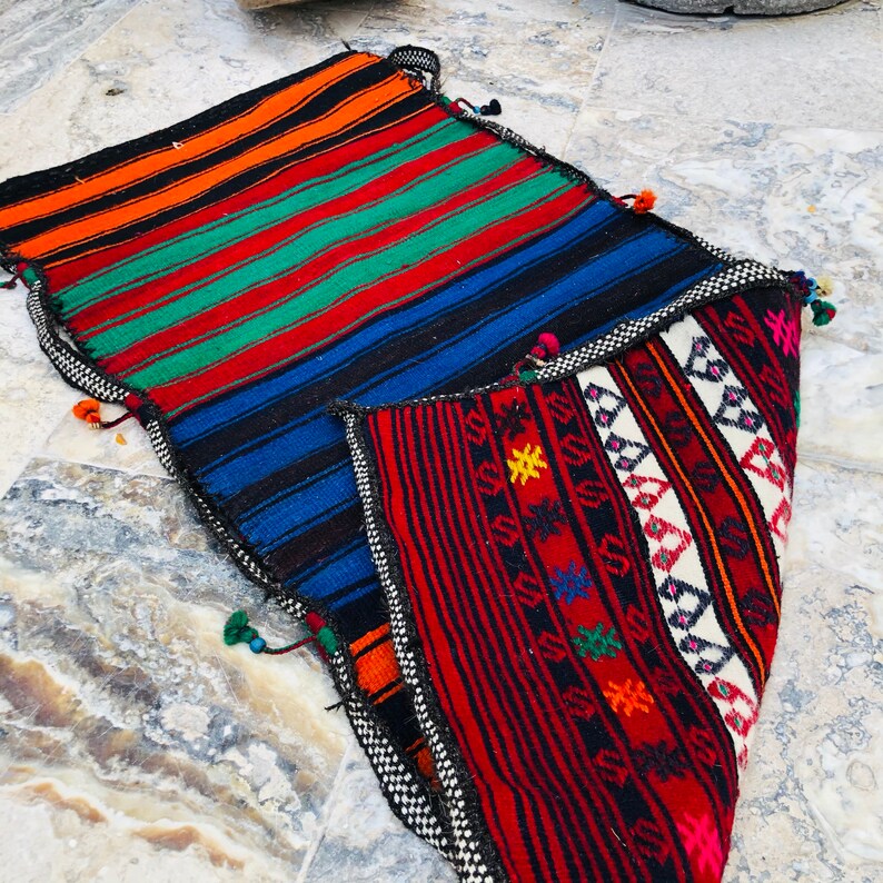 May include: A colorful woven rug with a geometric pattern in shades of red, blue, green, orange, and white. The rug is folded in half, revealing the intricate details of the design.