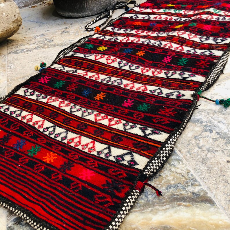 May include: A long, narrow, red, black, and white woven rug with geometric patterns. The rug has a fringe on both ends.
