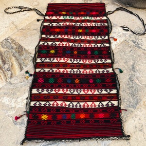 May include: A long, narrow, red, black, and white woven rug with colorful geometric patterns and tassels on the edges.