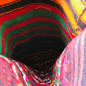 May include: A close-up of the inside of a woven rug. The rug is made of colorful stripes of red, green, orange, and black wool. The rug is folded in on itself, creating a tunnel-like shape.