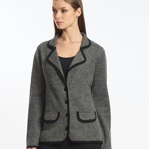 Könnte beinhalten: Ein schwarz-weiß gemusterter Blazer mit schwarzem Besatz und Knopfverschluss. Der Blazer wird über einem schwarzen Tanktop und einer schwarzen Hose getragen. Die Person trägt schwarze Stiefeletten.