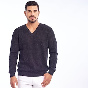 Puede incluir: Un suéter gris oscuro de cuello en V con mangas largas y un hombre con jeans blancos y zapatillas negras.