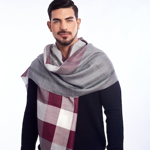 Puede incluir: Un hombre con un suéter negro y pantalones blancos con una bufanda de cuadros grises y burdeos alrededor del cuello.