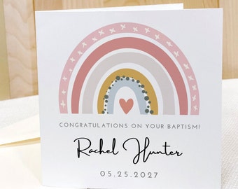 May include: A white card with a rainbow design in pink, gray, and yellow with a small heart in the center. The text "Congratulations on your Baptism! Rachel Hunter 05.25.2027" is printed on the card.