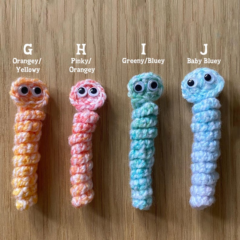 K&ouml;nnte beinhalten: Vier geh&auml;kelte Wurmspielzeuge mit Glitz Augen. Die W&uuml;rmer sind orange, rosa, gr&uuml;n und blau.