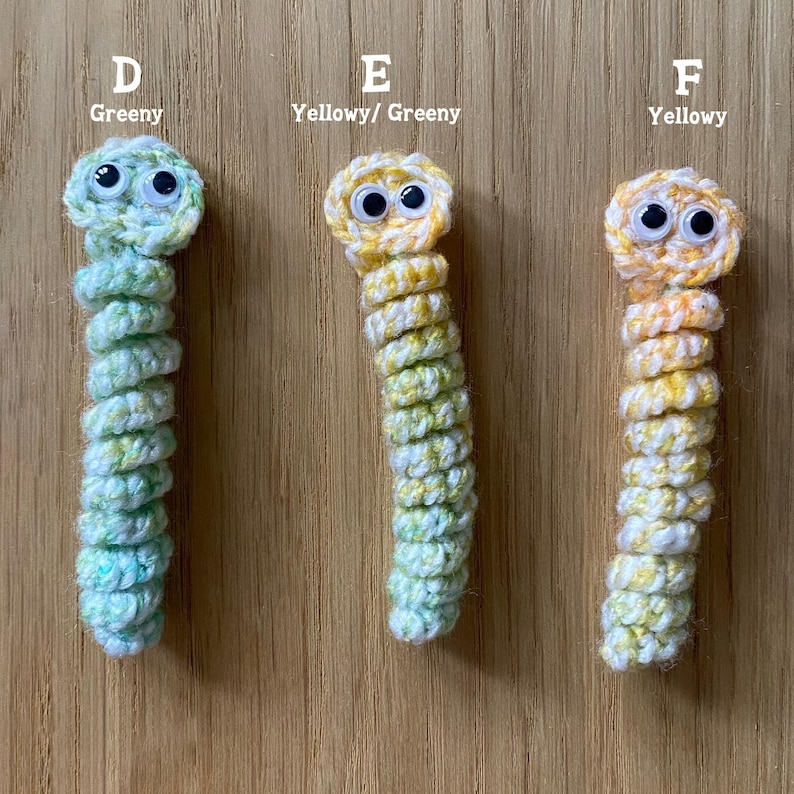 K&ouml;nnte beinhalten: Drei geh&auml;kelte Wurmspielzeuge mit Glitz Augen. Der erste Wurm ist gr&uuml;n und wei&szlig;, der zweite ist gelb und gr&uuml;n, und der dritte ist gelb und wei&szlig;.
