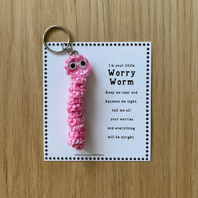 K&ouml;nnte beinhalten: Rosa geh&auml;kelter Sorgenwurm Schl&uuml;sselanh&auml;nger mit Glitzern und einer wei&szlig;en Karte mit der Aufschrift "Ich bin dein kleiner Sorgenwurm. Halte mich in deiner N&auml;he und dr&uuml;cke mich fest, erz&auml;hl mir all deine Sorgen und alles wird gut."