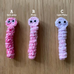 K&ouml;nnte beinhalten: Drei geh&auml;kelte Wurmspielzeuge in verschiedenen Rosat&ouml;nen. Der Wurm links ist dunkelrosa, der mittlere Wurm ist rosa und der Wurm rechts ist hellrosa. Jeder Wurm hat Glitz Augen.