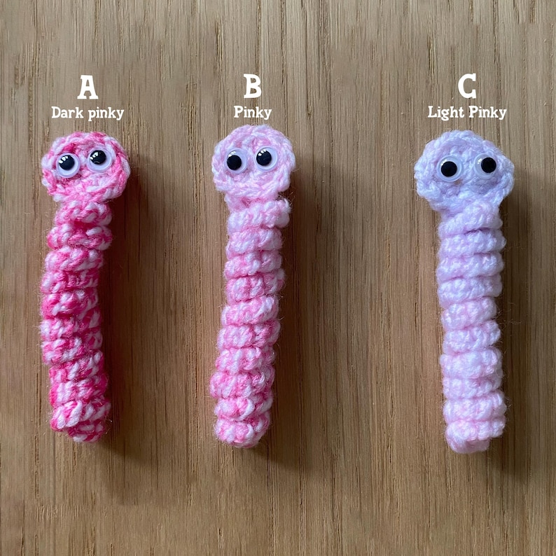 K&ouml;nnte beinhalten: Drei geh&auml;kelte Wurmspielzeuge in verschiedenen Rosat&ouml;nen. Der Wurm links ist dunkelrosa, der mittlere Wurm ist rosa und der Wurm rechts ist hellrosa. Jeder Wurm hat Glitz Augen.