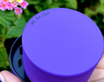 May include: Purple grinder with the text "9th Ave Club" on the top. The grinder is open and the bottom part is visible.