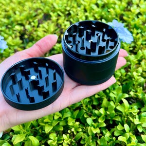 May include: A black metal grinder with a removable top. The grinder has a series of teeth for grinding herbs.