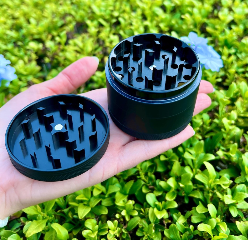May include: A black metal grinder with a removable top. The grinder has a series of teeth for grinding herbs.