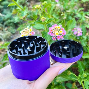 Puede incluir: Triturador de metal morado con tapa negra y mecanismo de molienda de metal negro. El triturador est&aacute; abierto y la tapa est&aacute; colocada al lado.