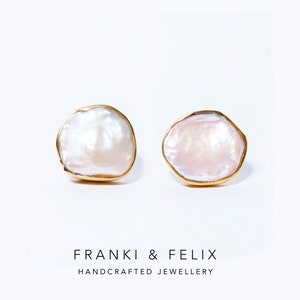 Op de afbeelding: Een paar goudomrande oorbellen met onregelmatige, witte en roze getinte parelcentra. De oorbellen staan tegen een witte achtergrond. De tekst "FRANKI & FELIX HANDCRAFTED JEWELLERY" staat onderaan.