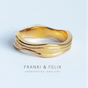 May include: A gold ring with a flowing, organic design. The ring's surface is polished and features delicate ridges. The text "FRANKI & FELIX HANDCRAFTED JEWELLERY" is printed below the ring.